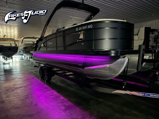 Barletta Pontoon A sleek black pontoon boat with purple LED lighting in a showroom.
